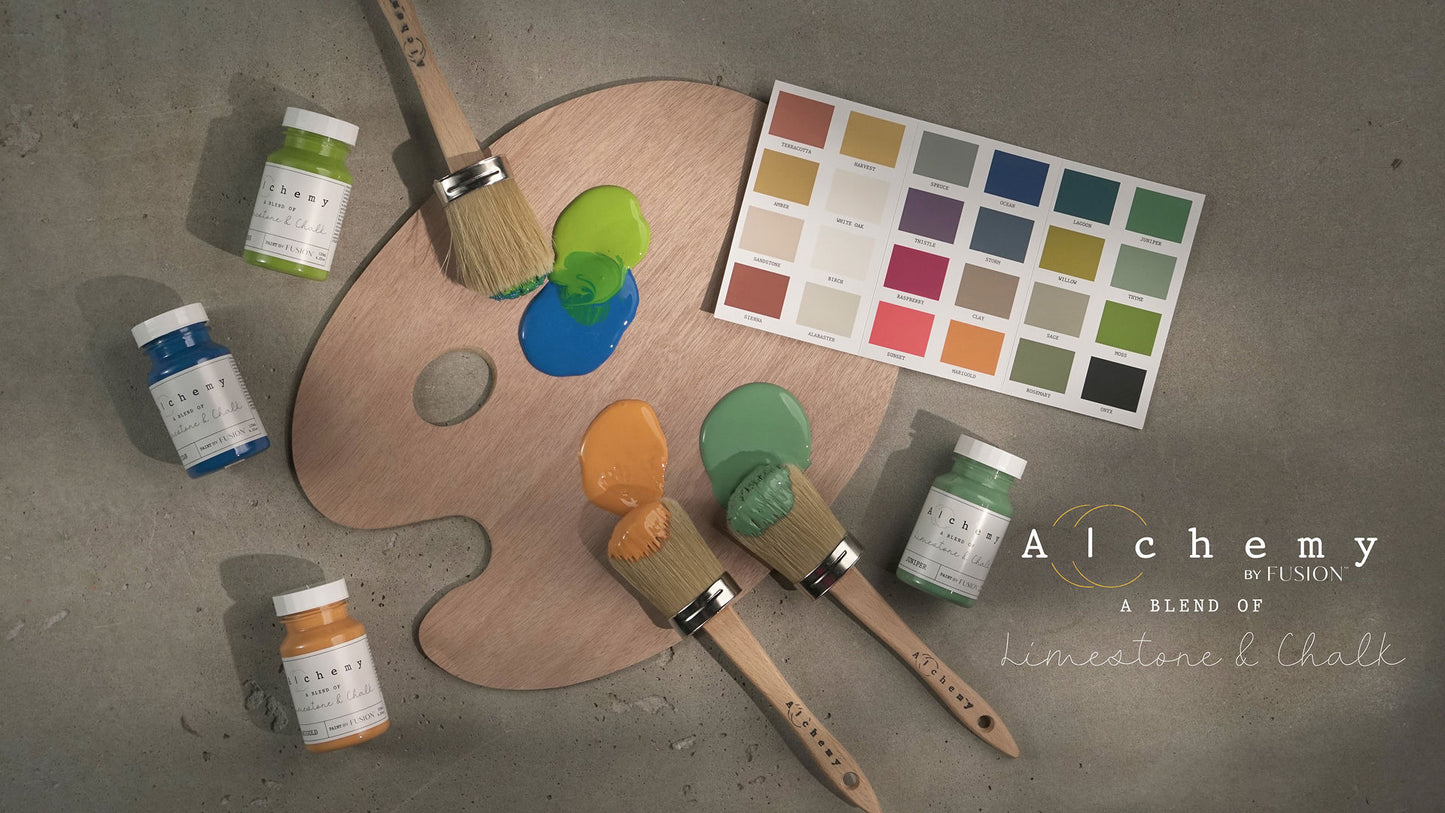 Composición artística con botes de pintura Alchemy by Fusion, brochas y carta de colores sobre paleta de pintor, colección limestone y chalk