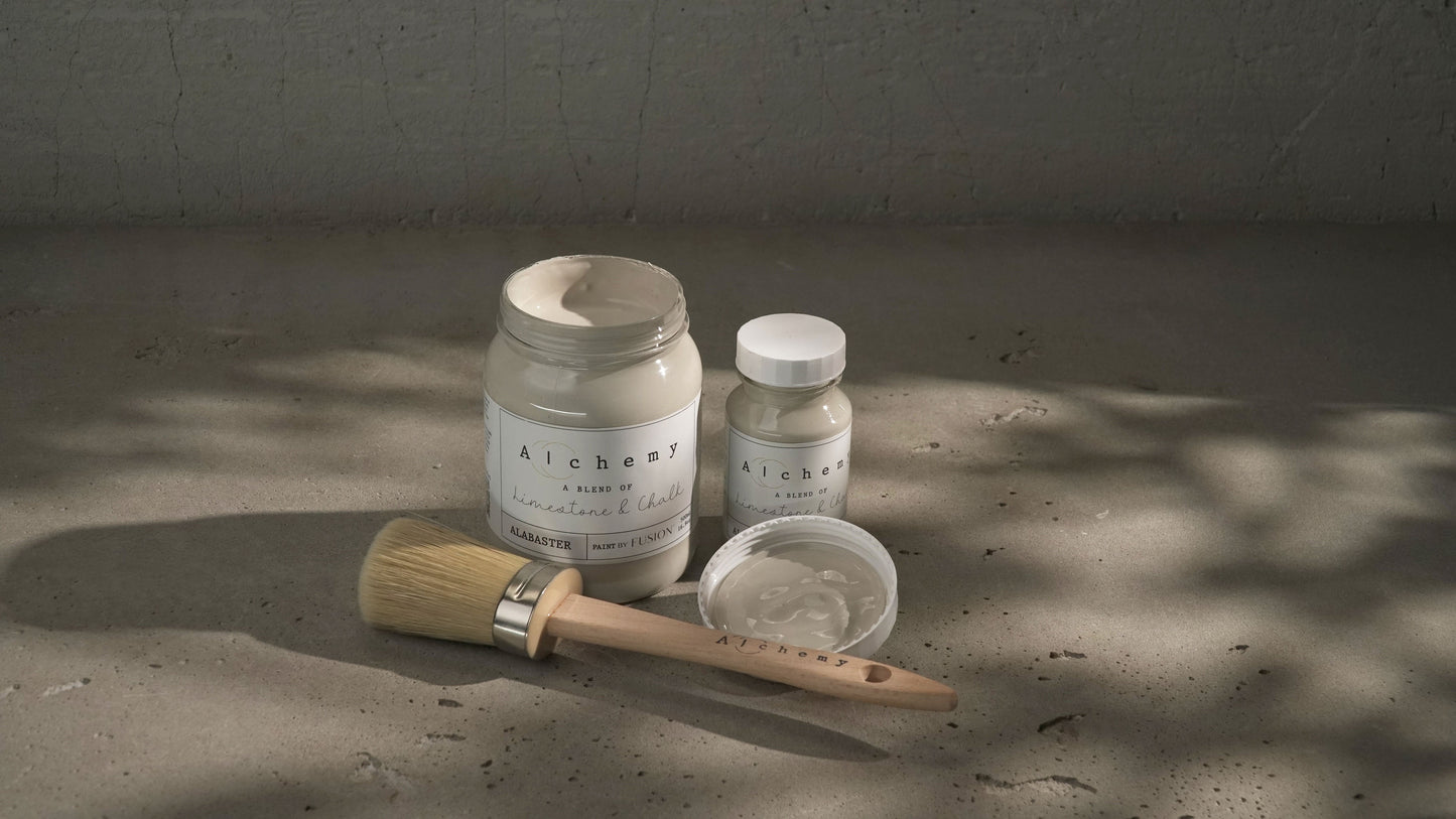 Botes Alchemy by Fusion Alabaster 500ml y 120ml con brocha sobre superficie de cemento, pintura a la tiza taupe sereno