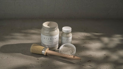 Botes Alchemy by Fusion Alabaster 500ml y 120ml con brocha sobre superficie de cemento, pintura a la tiza taupe sereno