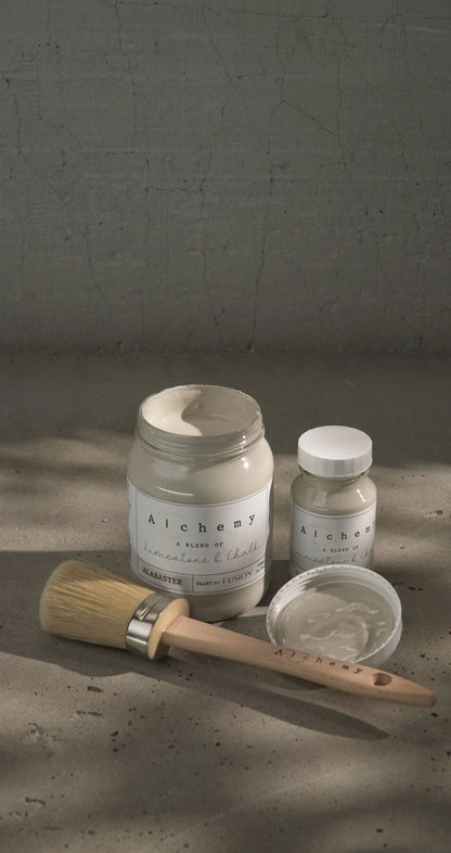 Botes Alchemy by Fusion Alabaster 500ml y 120ml con brocha sobre superficie de cemento, vista vertical, pintura a la tiza greige elegante