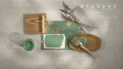 Flatlay inspiracional Alchemy by Fusion Juniper con muestra de color, brocha redonda, bote 120ml y elementos naturales sobre fondo de azulejo