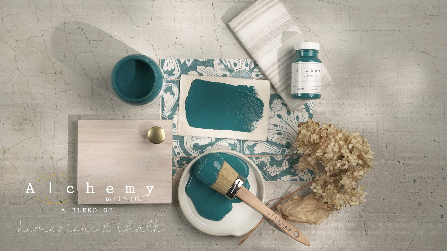 Flatlay inspiracional Alchemy by Fusion Lagoon con muestra de color, brocha redonda, bote 120ml y elementos naturales sobre fondo de azulejo