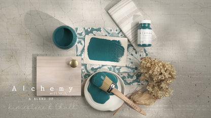 Flatlay inspiracional Alchemy by Fusion Lagoon con muestra de color, brocha redonda, bote 120ml y elementos naturales sobre fondo de azulejo