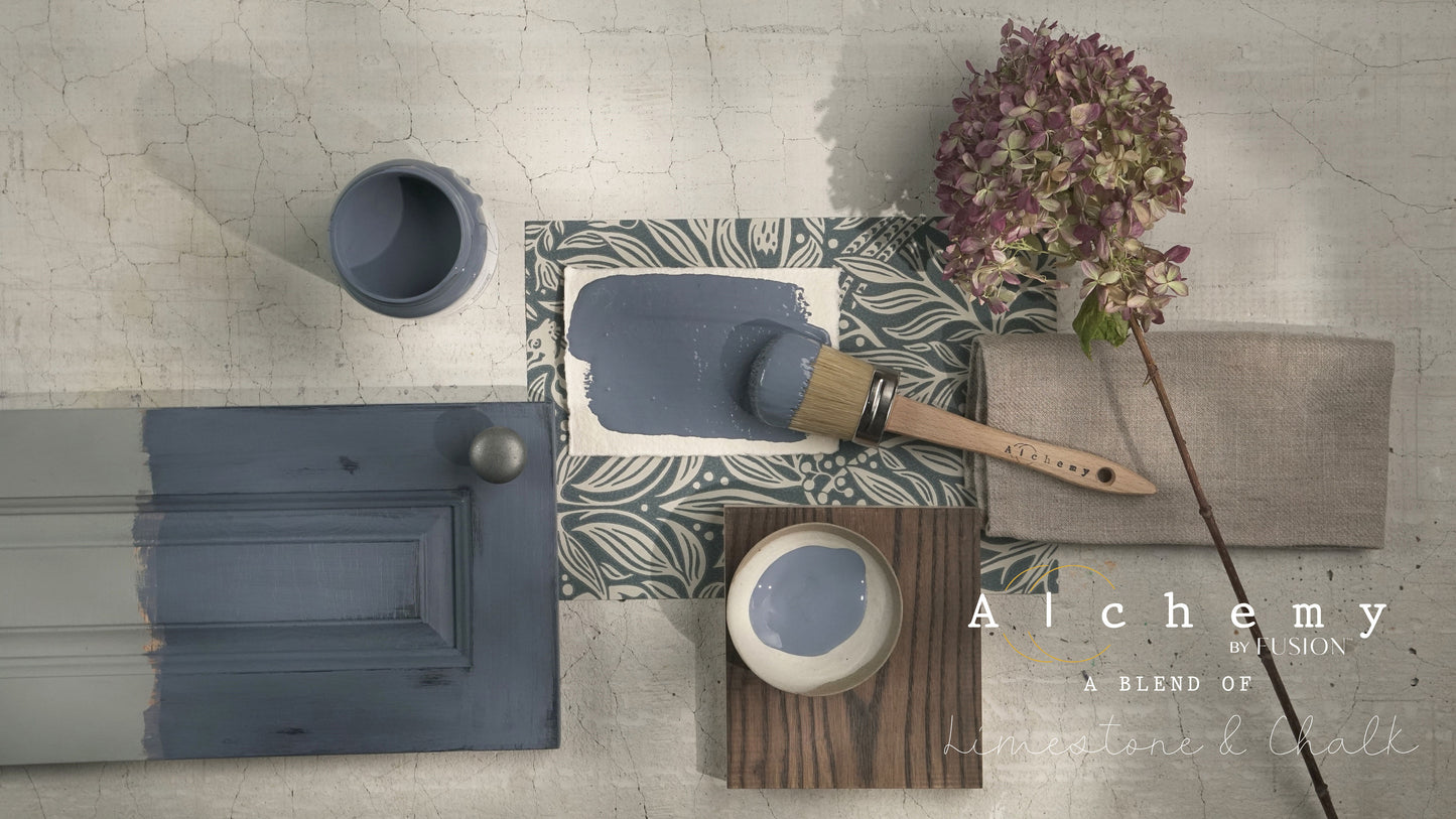 Flatlay inspiracional Alchemy by Fusion Storm con muestra de color gris lavanda, bote 120ml, brocha redonda, frente de cajón pintado, papel botánico y hortensia seca sobre fondo de azulejo craquelado