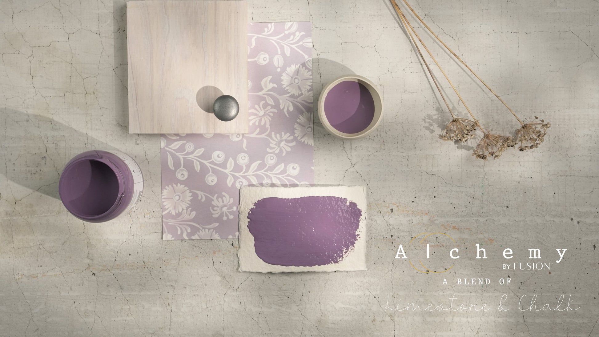 Flatlay inspiracional Alchemy by Fusion Thistle con muestra de color malva, botes abiertos, papel estampado floral, tirador cerámico gris y flores silvestres secas sobre fondo de azulejo craquelado