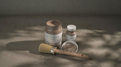 Botes Alchemy by Fusion Clay 500ml y 120ml con brocha redonda sobre superficie de cemento con sombras naturales, pintura a la tiza taupe gris cálido