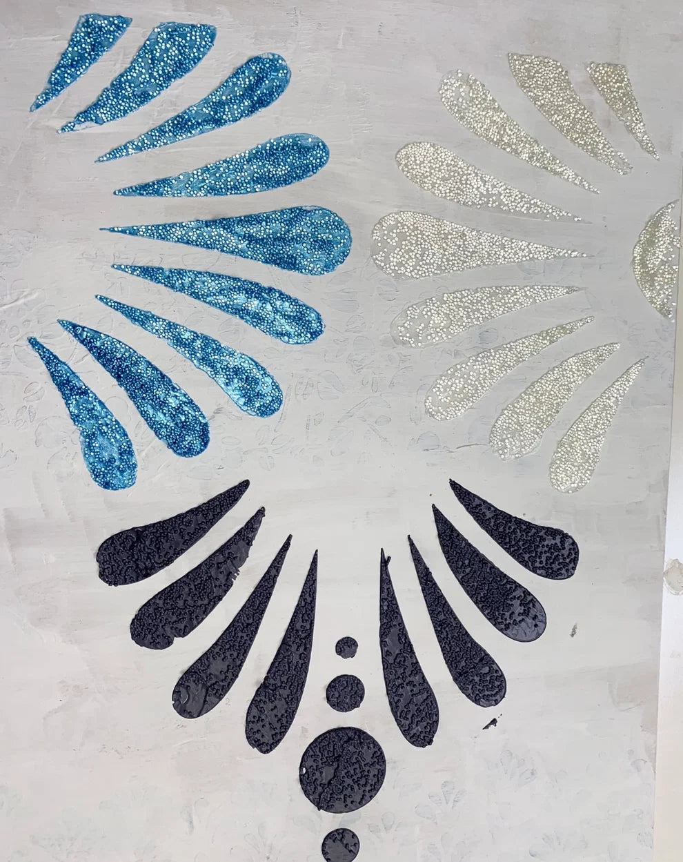 Detalle de Glass Bead Gel de Re-Design with Prima aplicado con stencil - motivo floral en azul, plata y negro con textura de microesferas de cristal sobre superficie blanca
