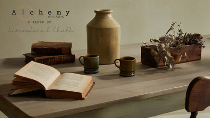 Mesa de escritorio vintage restaurada con Alchemy by Fusion Sage en verde salvia grisáceo con efecto desgastado, decorada con libros antiguos, jarra cerámica y tazas artesanales, pintura limestone y chalk

