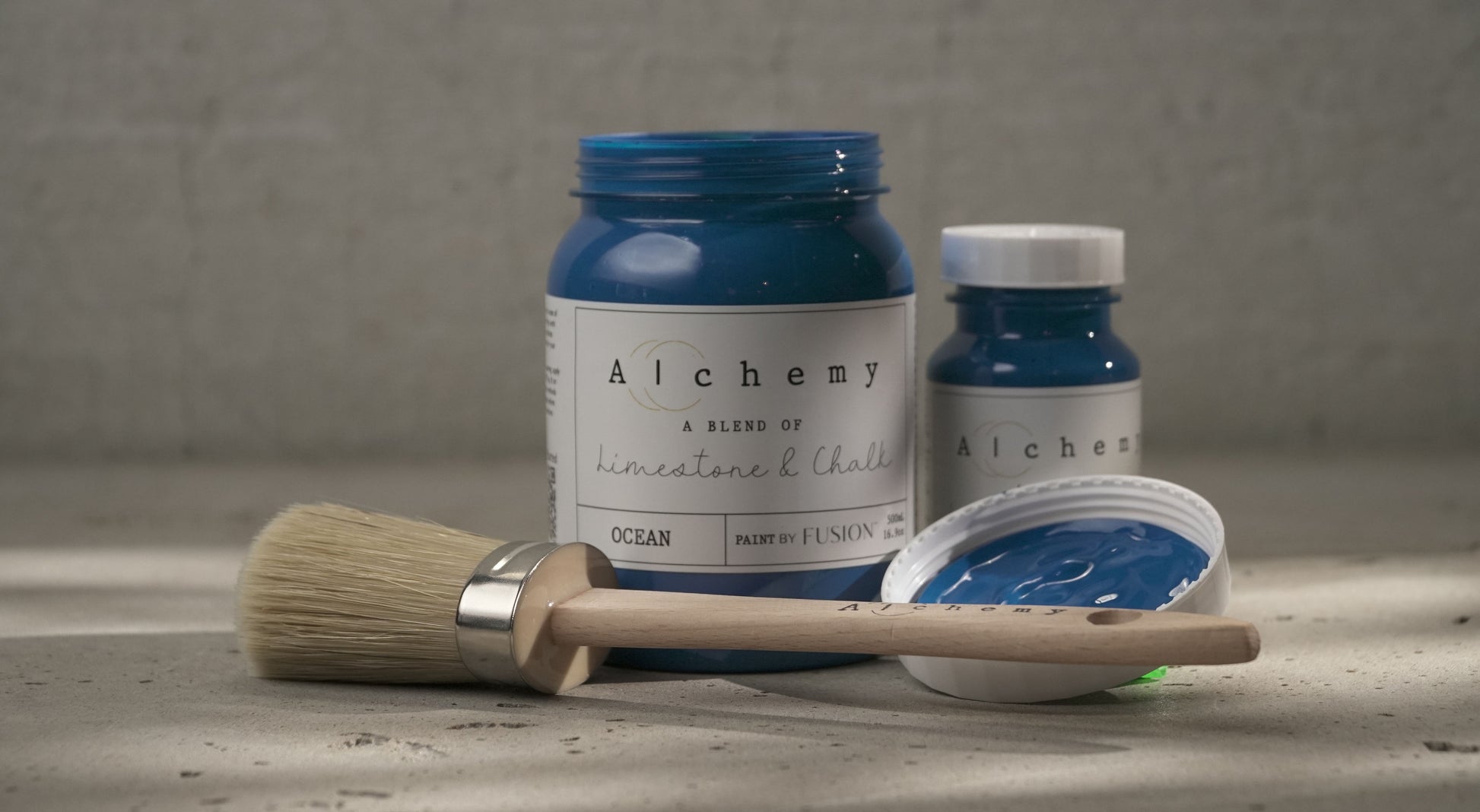 Botes Alchemy by Fusion Ocean 500ml y 120ml con brocha sobre superficie de cemento, pintura a la tiza azul marino intenso
