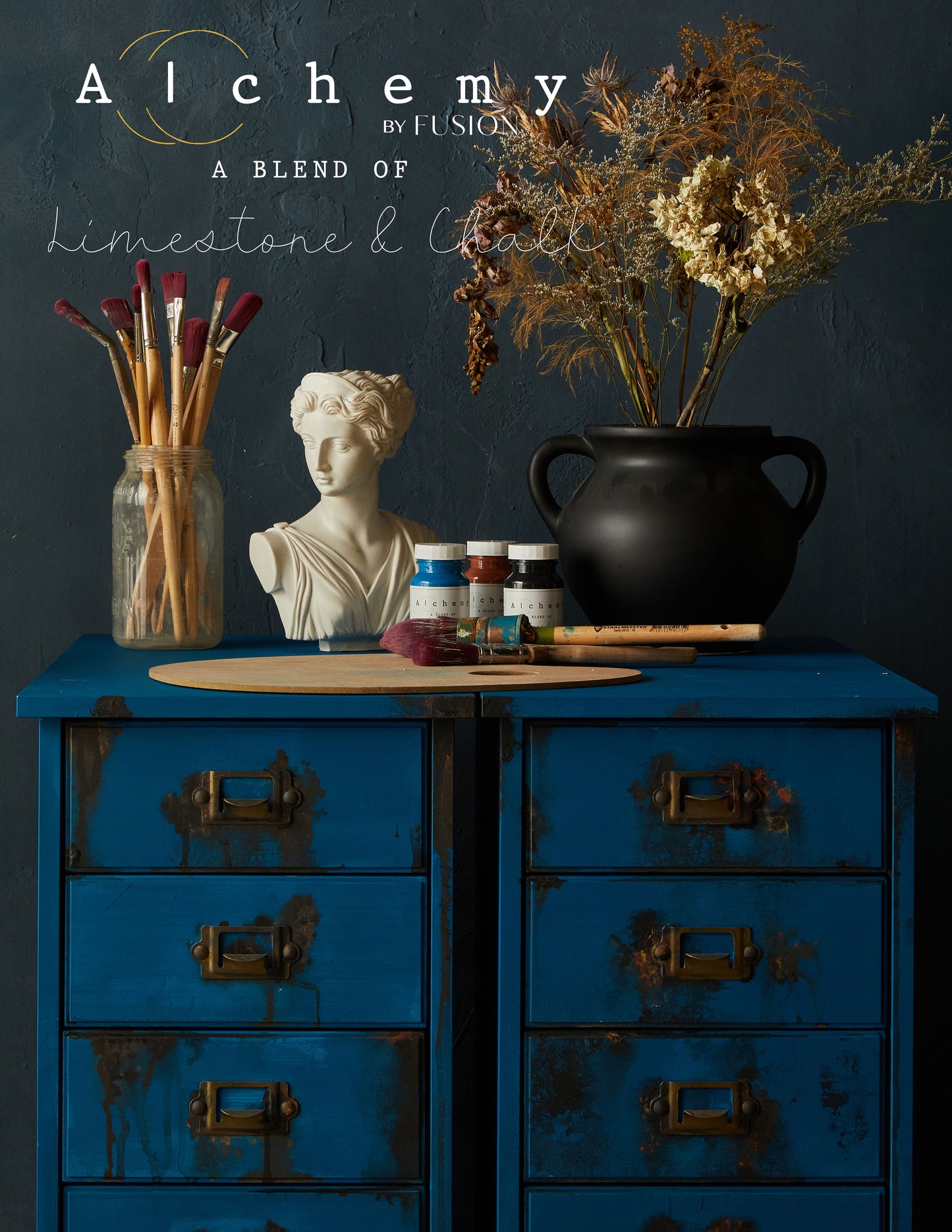 Detalle superior de cajonera restaurada con Alchemy by Fusion Ocean en azul marino, decorada con botes Alchemy, busto clásico y jarrón negro con flores secas