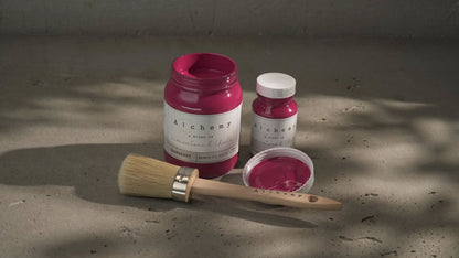 Botes Alchemy by Fusion Raspberry 500ml y 120ml abiertos con brocha redonda sobre superficie de cemento con sombras de luz natural, pintura a la tiza fucsia vibrante