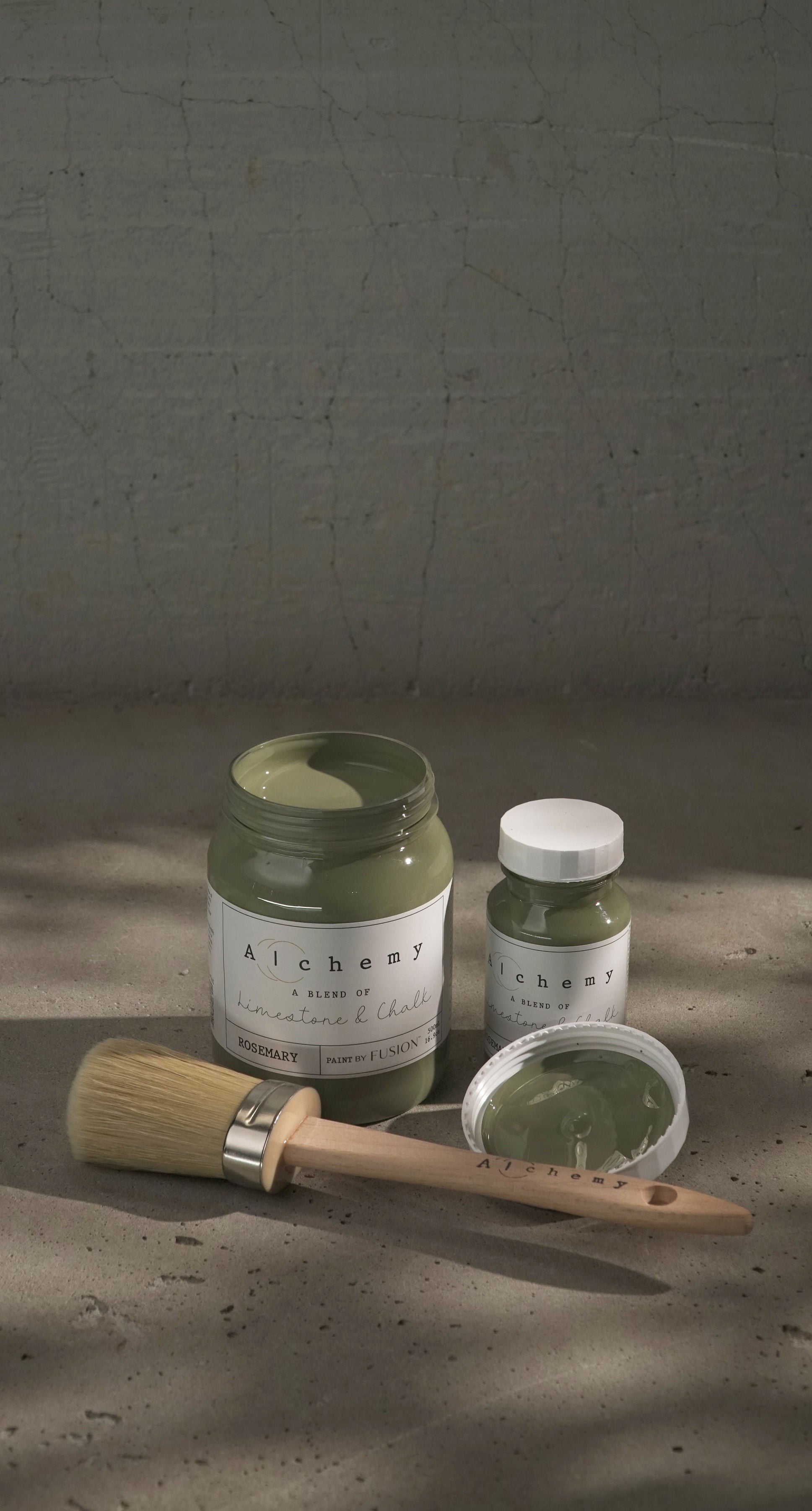 Botes Alchemy by Fusion Rosemary 500ml y 120ml abiertos con brocha sobre fondo de cemento texturizado con luz lateral, pintura a la tiza verde herbáceo limestone y chalk

