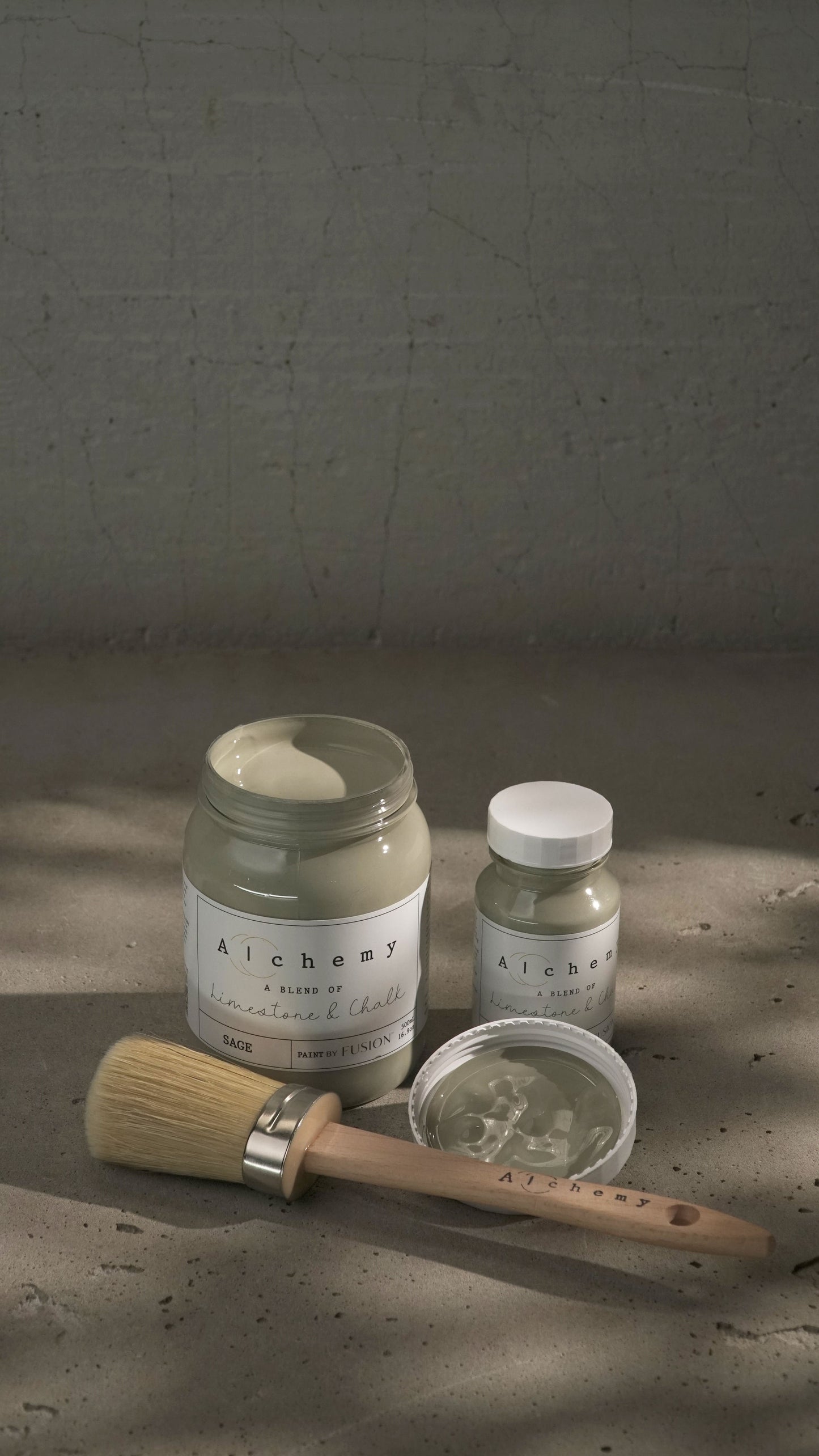 Botes Alchemy by Fusion Sage 500ml y 120ml con brocha sobre fondo de cemento texturizado, pintura a la tiza verde salvia limestone y chalk
