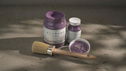 Botes Alchemy by Fusion Thistle 500ml y 120ml abiertos con brocha redonda sobre superficie de cemento con sombras de luz natural, pintura a la tiza malva profundo