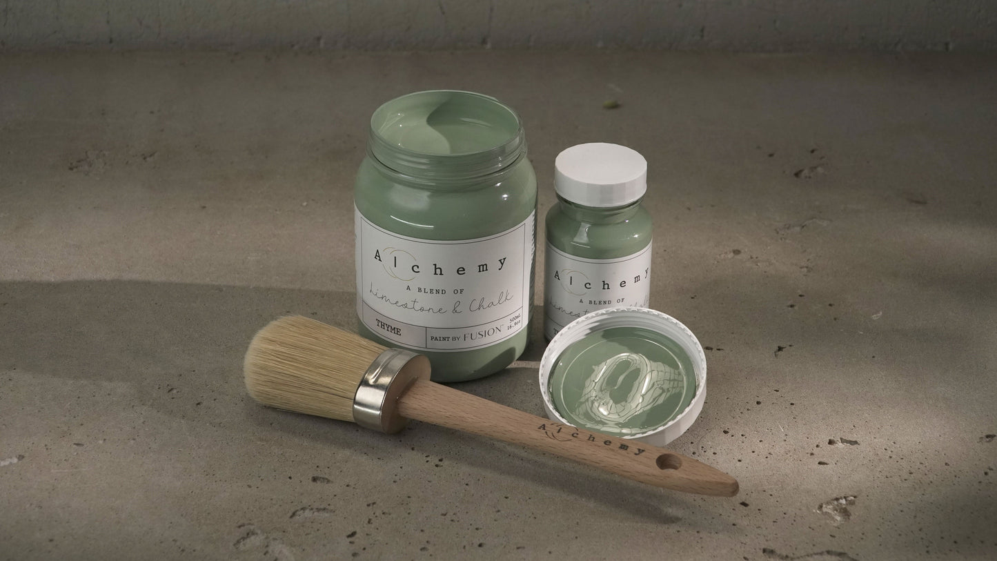 Botes Alchemy by Fusion Thyme 500ml y 120ml abiertos con brocha redonda y tapa sobre superficie de cemento con luz lateral, pintura a la tiza verde azulado fresco