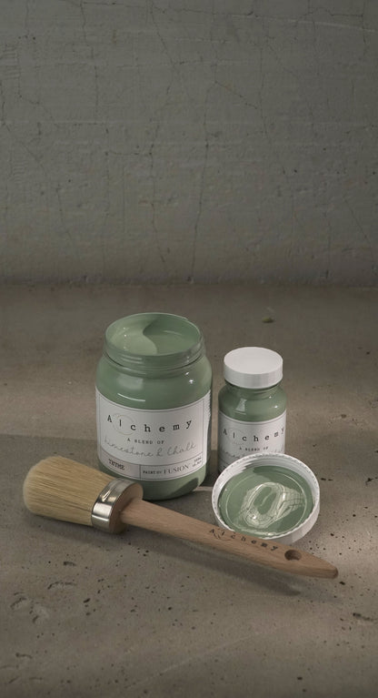 Botes Alchemy by Fusion Thyme 500ml y 120ml abiertos con brocha sobre fondo de cemento texturizado con luz cenital y sombras suaves, pintura a la tiza verde azulado limestone y chalk