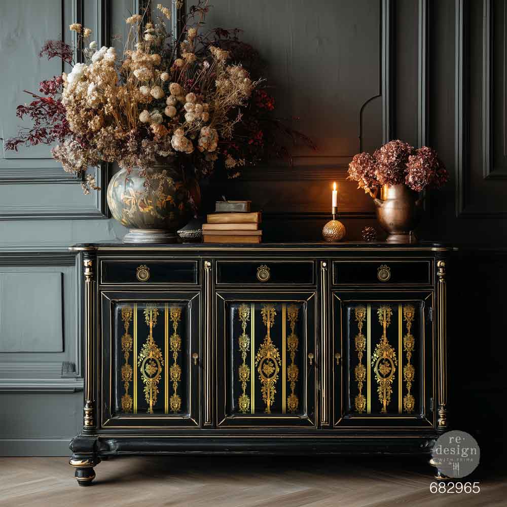 Transferencia Gold Foil Chateau Filigree Kacha en aparador negro lacado con cantos dorados y tiradores de anilla - medallones y franjas doradas en puertas, ambiente oscuro con flores secas y vela - Re-Design with Prima
