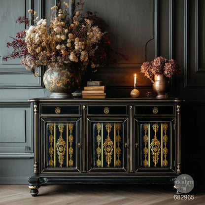 Transferencia Gold Foil Chateau Filigree Kacha en aparador negro lacado con cantos dorados y tiradores de anilla - medallones y franjas doradas en puertas, ambiente oscuro con flores secas y vela - Re-Design with Prima
