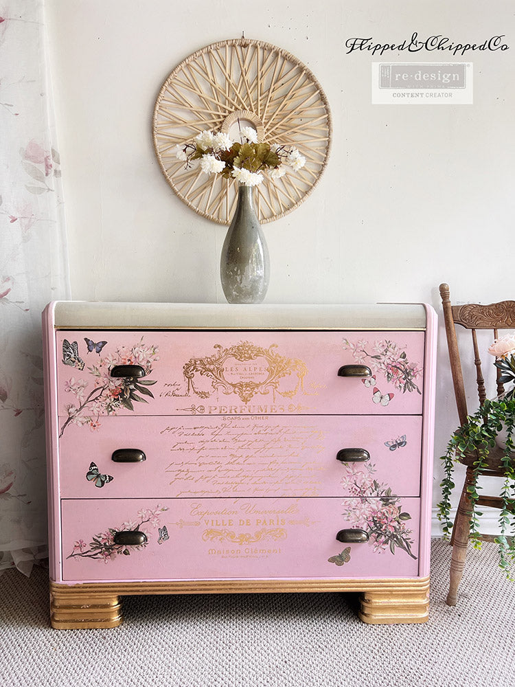 Transferencia decorativa Gold Foil Perfume Notes Kacha en cómoda rosa palo art déco restaurada - texto dorado Perfumes Ville de Paris con mariposas y flores en cajones, tiradores negros - Re-Design with Prima - ambassador Flipped and Chipped Co
